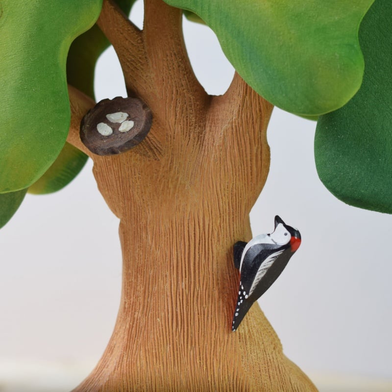 The Bumbu Handmade Wooden Large Oak Autumn and Woodpecker Set features a hand-painted oak tree with green leaves, a textured brown trunk, and a black, white, and red woodpecker near a nest with three white eggs in a hollow branch.