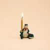 A handcrafted keepsake, the Later Gator Cake Topper features a ceramic alligator figurine wearing a red scarf and holding an upright lit candle in one hand, set against a plain beige background.