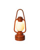 An orange Maileg Lantern with a glowing white light, featuring a rounded base and a metal handle loop. Resembling a miniature lantern, it has a classic, rustic design and is set against a plain white background.