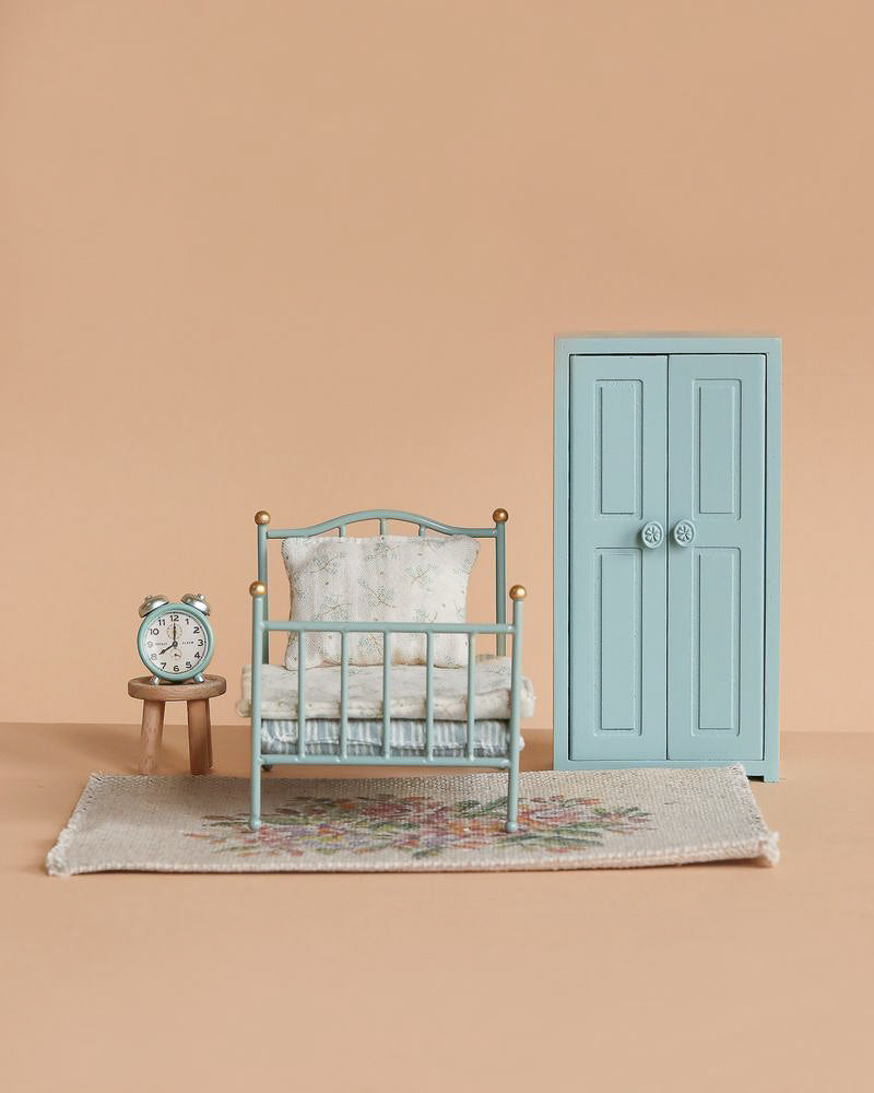 The Maileg Bedroom Set features a vintage bed, matching blue wardrobe, floral rug, alarm clock, and wooden stool—an adorable mouse furniture collection displayed against a soft beige background.
