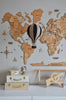 The Hot Air Balloon - Black, paired with a decorative wooden world map, travel-themed items like a globe, white suitcases, boxes, and a wooden airplane, creates the perfect decoration for a child's room.