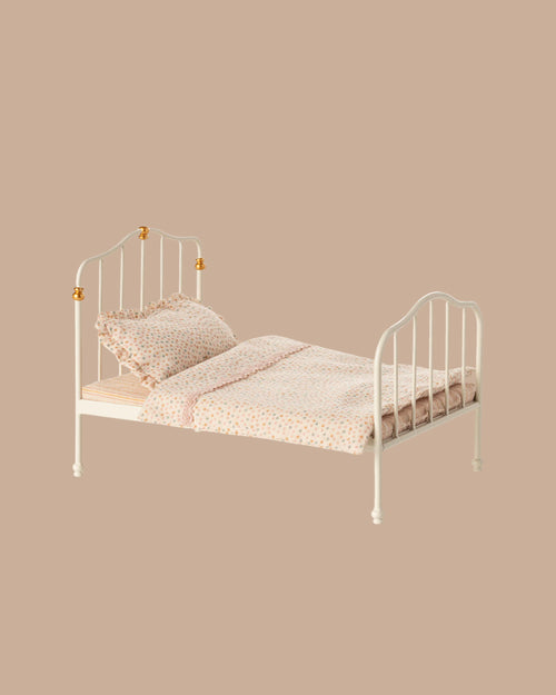 The PRE-ORDER: Vintage Bed, Mouse Size - Off White (ships early October), featuring a headboard and footboard, is dressed in light pink and white Maileg printed bedding with pillows, set against a plain beige background.