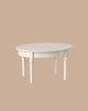 The PRE-ORDER: Vintage Dining Table, Mouse - Off White features a round white wooden design with detailed legs, showcased against a plain beige background. Estimated ship date is early October.