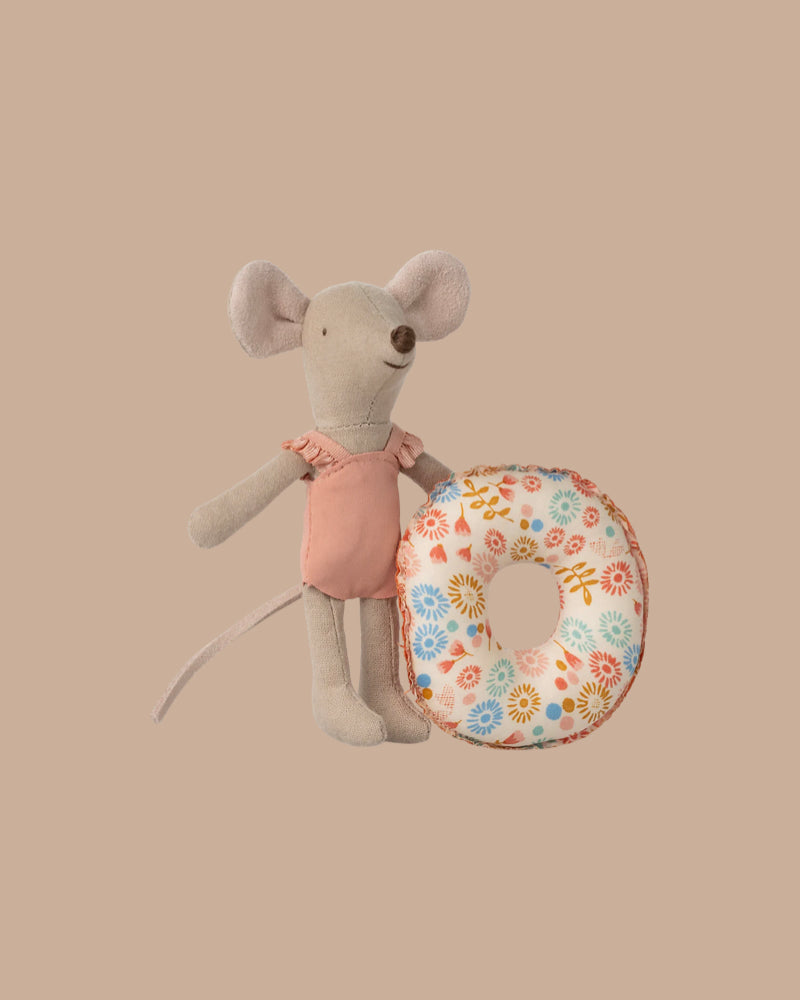 A Maileg Springtime Wardrobe Set mouse in a pink outfit stands upright, holding a floral-patterned floatation ring against a plain beige background.