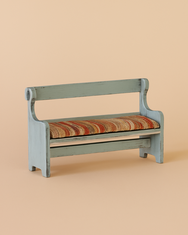 The Maileg Mouse Bench - Vintage Blue is a small, light blue wooden bench with a backrest and curved armrests. It has a vintage design and a striped orange, beige, and brown cushioned seat, displayed on a plain beige background.