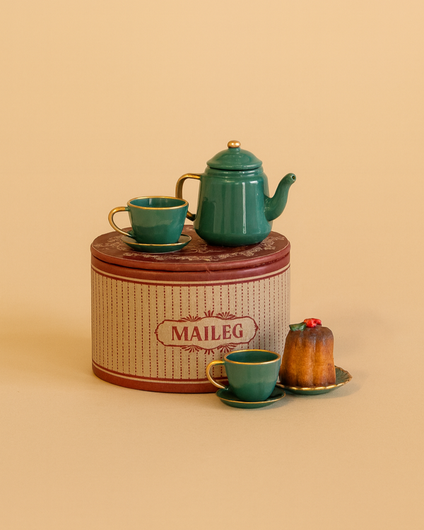 The Maileg Christmas Tea Party set features a small teal mouse family tea set with two matching teacups, saucers, a pastry, and a vintage-style round tin box in beige and maroon—ideal for miniature holiday tea parties.