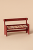 The Maileg Mouse Bench - Red is a small, hand-painted wooden bench with armrests and a backrest, featuring a striped cushion in beige, red, and green—ideal as charming mouse furniture—set against a plain beige background.