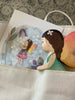The Handmade Holzwald Maya Fairy and Postcard are nestled in a white cloth bag, set against a patterned grey carpet that highlights the whimsical charm of these natural wooden toys.