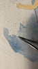 A close-up of a paintbrush applying blue watercolor around white star shapes on paper, with part of a drawing of an arm and dress visible at the top, evokes the delicate artistry found in the Handmade Holzwald Maya Fairy and Postcard.