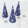 Three Meri Meri Wizard Party Hats, cone-shaped and with silver star and moon patterns, are arranged together on a white surface. Next to the hats are three silver star-shaped wands with wooden handles. One of the wands has a string attached, making them perfect for your next magic party or as wizard party supplies.