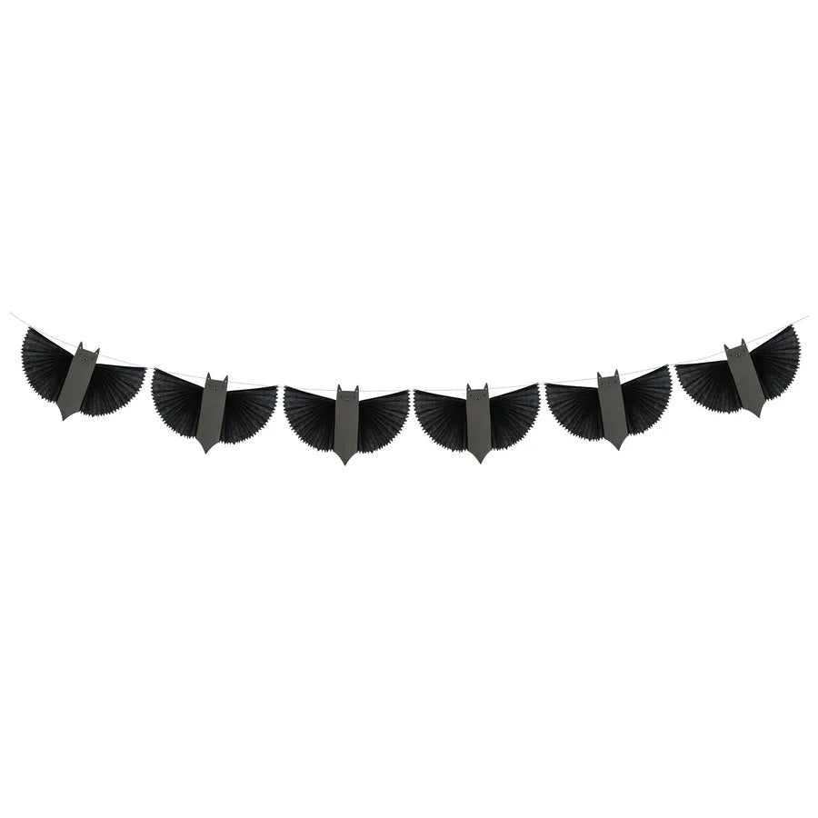 A black Meri Meri Bat Garland - Final Sale is strung across the image, featuring eight wing-like shapes evenly spaced along the length. Each shape appears to be made of a series of radiating thin lines, creating a stylish and symmetrical pattern reminiscent of paper bats.