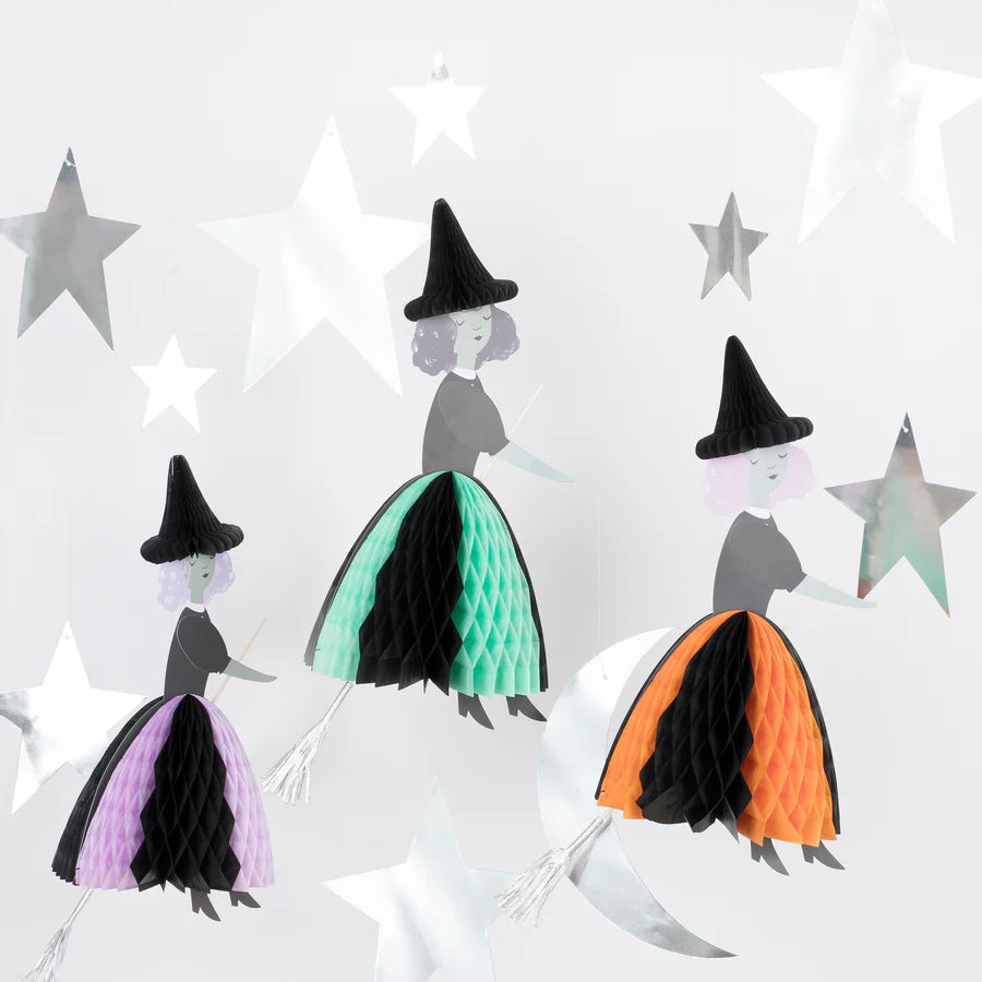 The Meri Meri Flying Honeycomb Witch Decorations - Final Sale feature three paper witches, each donning black pointy hats and holding white broomsticks. They hang amidst silver star cutouts, with their honeycomb skirts in green, purple, and orange, bringing a festive and whimsical charm that's perfect for your Halloween party decor.