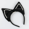 The Meri Meri Cat Costume headband features plush black cat ears outlined in faux pearls, ideal for Halloween costumes. Shown against a light gray background.