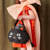 A child dressed in an orange outfit with a large, peach-colored bow draped over their shoulder holds the Trick Or Treat Cat Basket—designed to look like a cat's face, complete with cartoonish eyes, whiskers, and ears—perfect for a Halloween gift or trick-or-treating.