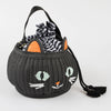 The Trick Or Treat Cat Basket, a delightful black basket bag designed to resemble a cat's face with embroidered green eyes, white whiskers, and an orange nose, features a black handle and includes a tucked-in black and white striped drawstring bag. Perfect as a trick or treat bag for Halloween or as an enchanting Halloween gift.