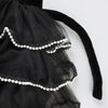 A close-up of layered black tulle fabric with ruffled edges, white pearl trim, and part of a black velvet bow from the Meri Meri Cat Costume—perfect for a whimsical Halloween look.