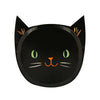 The Meri Meri It's Halloween! Plates are black paper plates designed to resemble a cat's face, perfect for Halloween. They feature green eyes, an orange nose and mouth, whiskers, and pointed ears with orange inner ear details. The background is plain white.