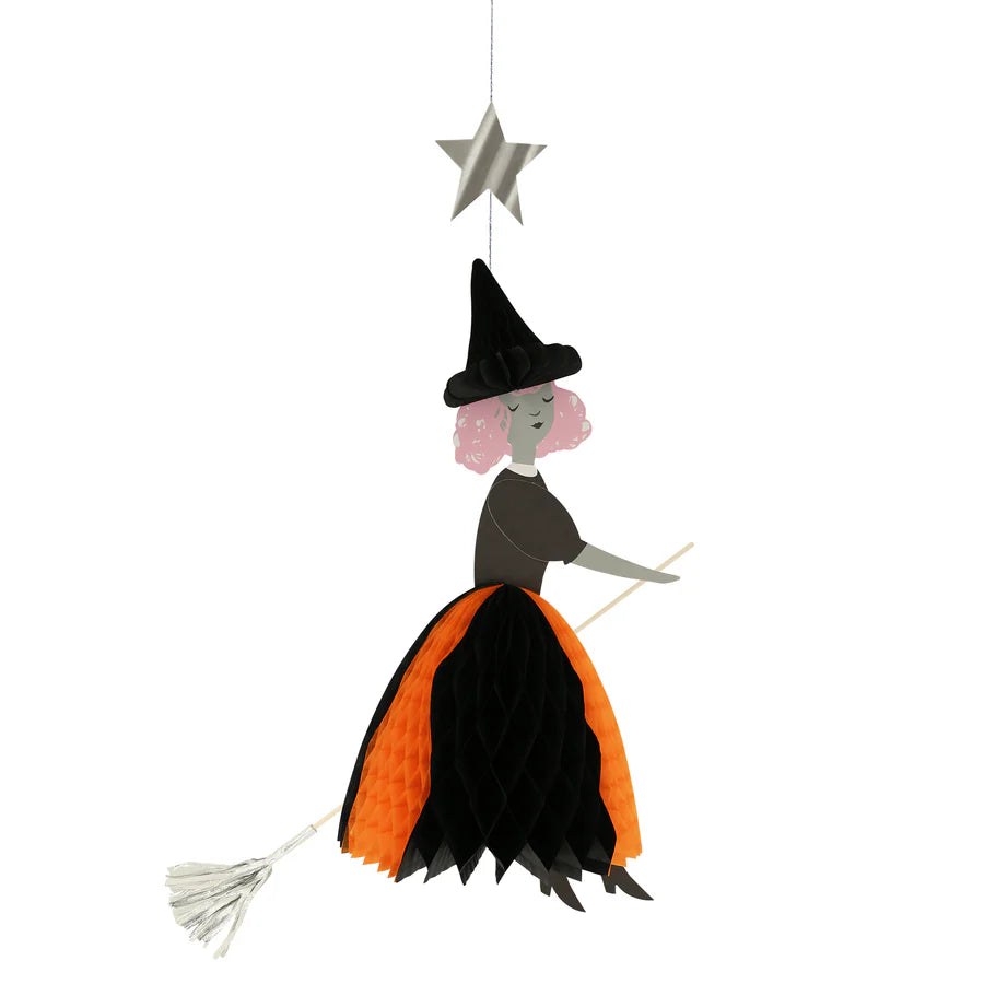 The Meri Meri Flying Honeycomb Witch Decoration is a perfect hanging ornament for your Halloween party decor, featuring a paper witch with pink hair wearing a black hat and an orange and black dress. She rides a broomstick and is suspended by a string attached to a silver star above her. Note that this item is on final sale.