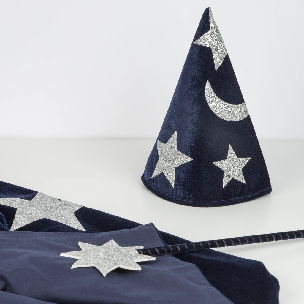 The Meri Meri Blue Velvet Wizard Costume—Final Sale—features a dark blue hat with silver glitter stars and a crescent moon, matching wand, and blue velvet cape, all displayed on a white surface for magical dress-up.