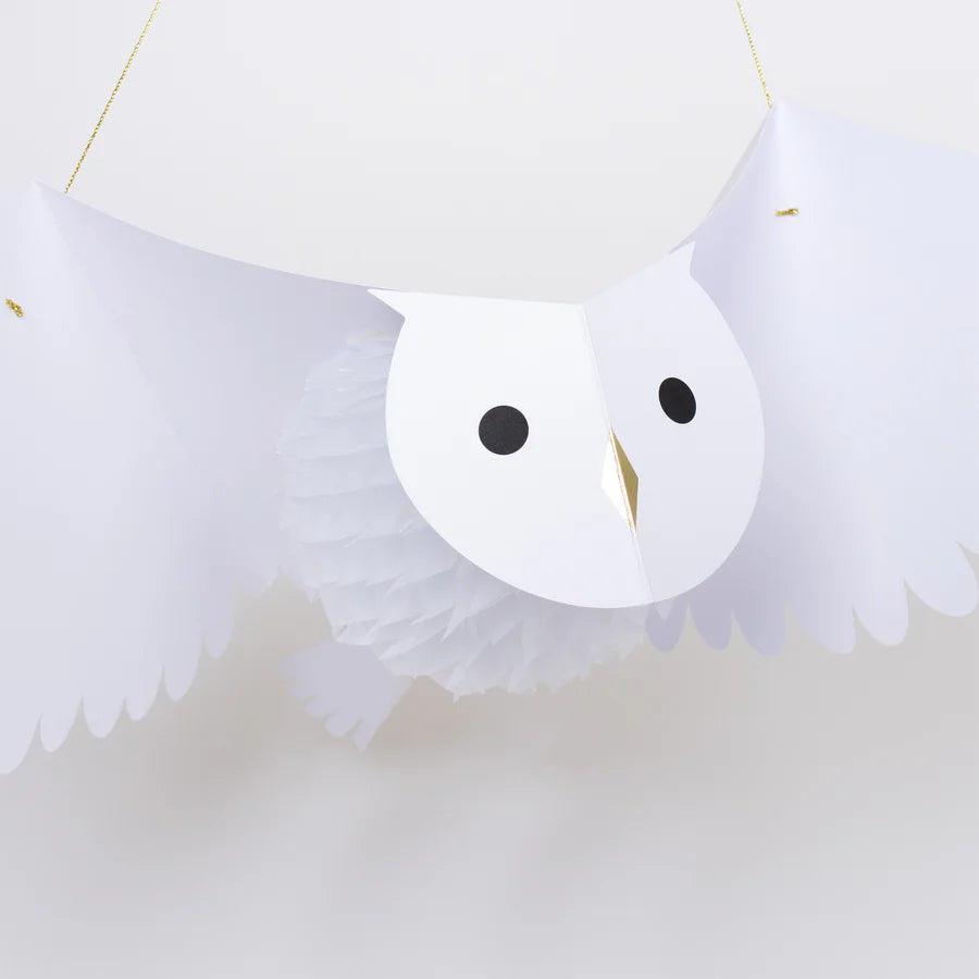 The Meri Meri Honeycomb Owl is a hanging white paper decoration featuring an owl with wide, spread wings. The owl has striking black round eyes, a simple gold beak, and intricate paper folds that form its body, giving it a three-dimensional appearance. This enchanting party decoration stands out beautifully against the plain white background.