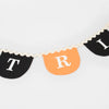 The Meri Meri Trick Or Treat Fabric Garland is a festive, reusable party decoration with alternating black and orange pennants that showcase the letters "T", "R", and "I" in white. This Halloween fabric garland is elegantly bordered with a wavy, cream-colored trim and set against a plain white background.