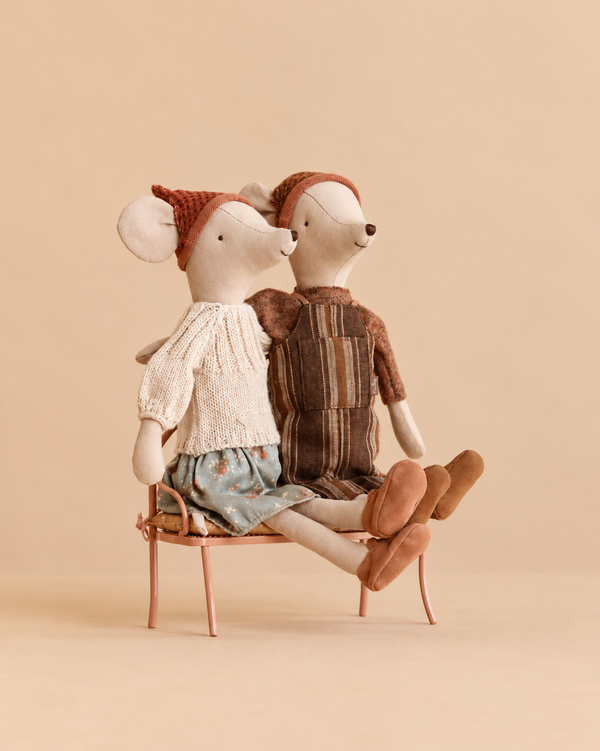 Two Maileg Medium Mice Set stuffed toys wearing knitted hats and outfits sit together on a small vintage metal bench.