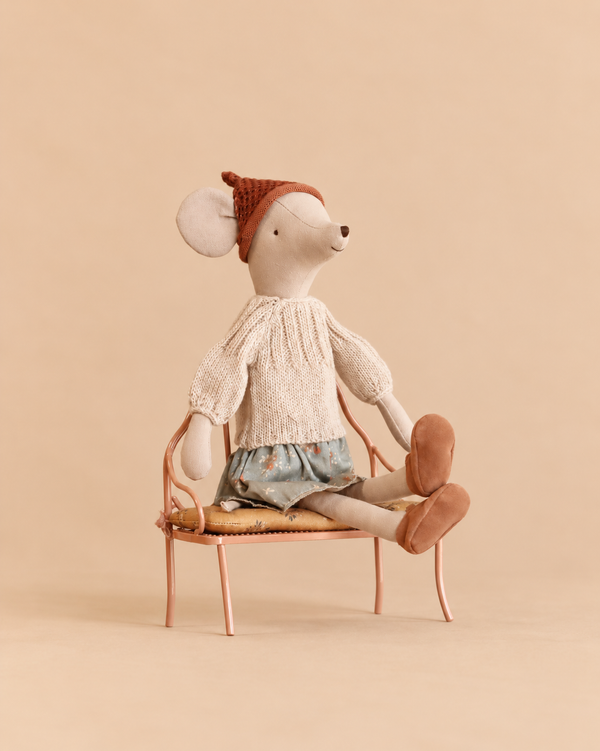 A Maileg Medium Mouse Set wearing a knitted sweater, floral skirt, and rust-colored cap, sitting on a vintage metal bench.