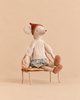 A Maileg Medium Mouse Set wearing a knitted sweater, floral skirt, and rust-colored cap, sitting on a vintage metal bench.
