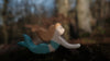 The Handmade Holzwald Mermaid features a small wooden figure with a blue tail and beige hair, resting on the forest floor with blurred trees behind—an ideal choice for open-ended play.
