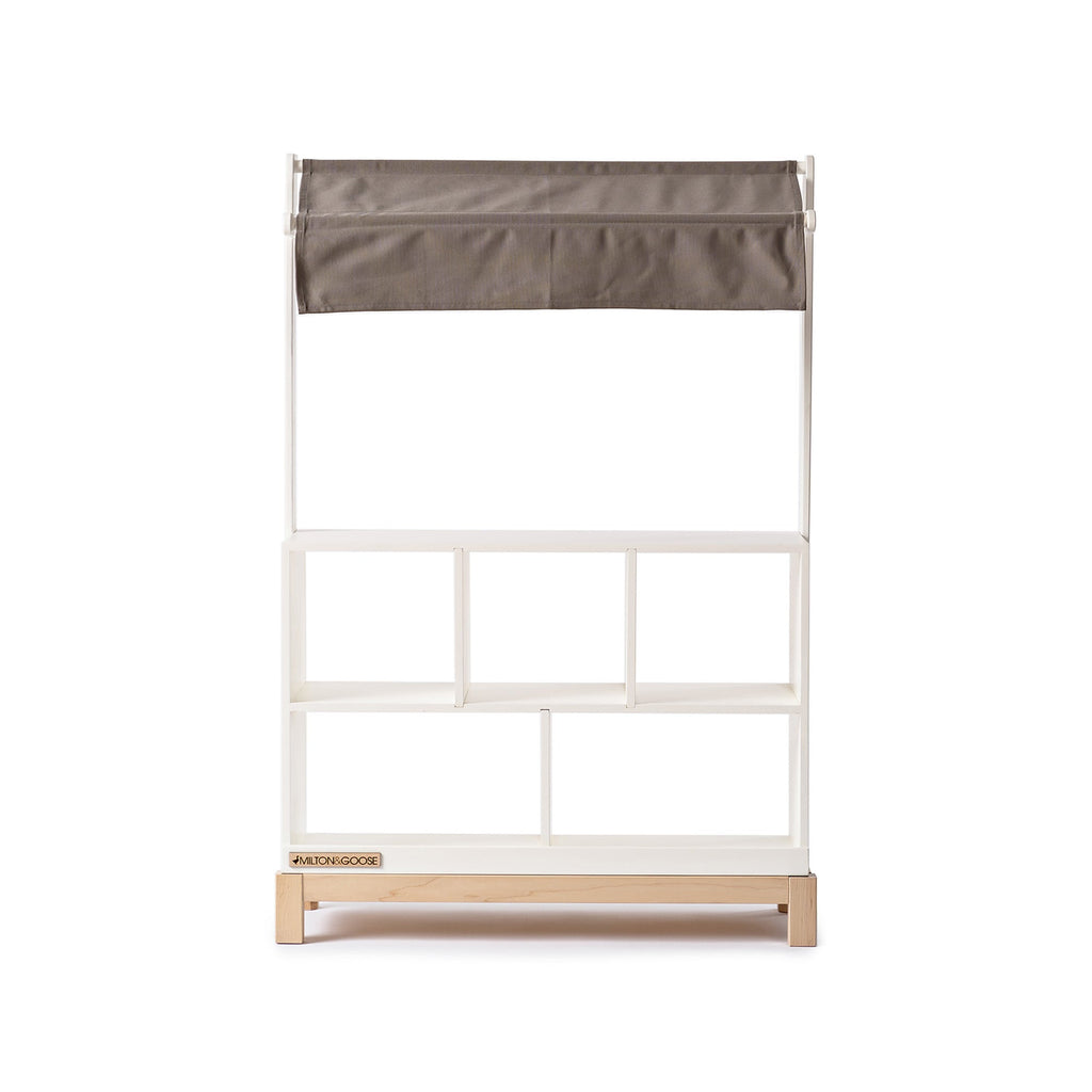 The Milton & Goose Market Stand is a handcrafted kids play shop, with a light brown fabric canopy, three open shelves, and a small wooden base—perfect for imaginative play. Shown isolated on a white background.