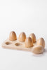 A wooden board featuring six slots, each holding a Milton & Goose Wooden Half Dozen Egg from Amish crafted toys. The board and eggs have a smooth, light wooden finish, set against a plain white background.