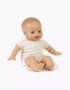 A Minikane Soft Body Doll (11") - Léo with a smooth bald head, light skin, and expressive facial features, showing an open mouth and wide eyes. Dressed in a white one-piece outfit, this doll is perfect for imaginative playtime or as a cozy bedtime companion, posed seated with legs extended and arms slightly outwards.