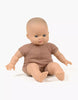 Introducing the Minikane Soft Body Doll (11") - Maé for imaginative playtime! This seated baby doll features a bald head, blue eyes, and a neutral facial expression. It boasts phthalate-free vinyl head, arms, and legs with a comfy fabric torso, dressed in a light brown outfit. The background is plain white.