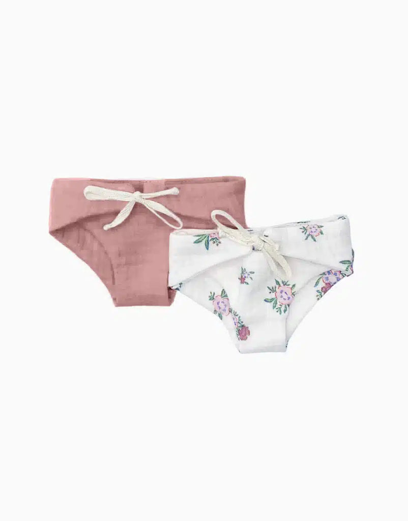 Two pairs of children's underwear on a white background. The pair on the left is solid pink with a white drawstring bow. The pair on the right is white with a floral pattern and also features a white drawstring bow, perfect for Minikane Doll Clothing | Set of 2 Diapers in Petal Pink and Floral or as double gauze diapers for 28cm dolls.