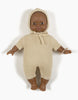 A dark-skinned Minikane Babies doll with short curly hair is wearing a Minikane Doll Clothing | Élie Cream Knit Bonnet. The doll, barefoot, is posed with its arms slightly out to the sides and its legs straight, lying on a white background.