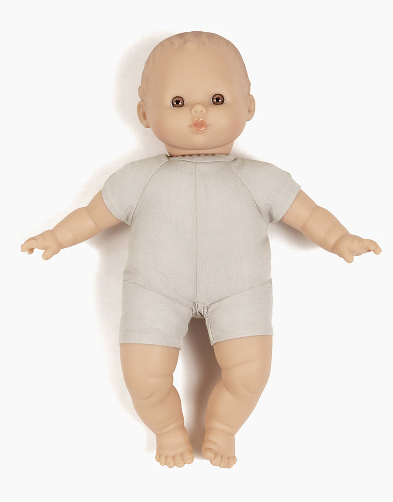 The Minikane Soft Body Doll (11") - Alice features a neutral expression, light skin tone, short blonde hair, and brown eyes. Crafted from phthalate-free vinyl for safe imaginative playtime, it wears a short-sleeve light gray onesie while laying on its back with arms and legs slightly spread.