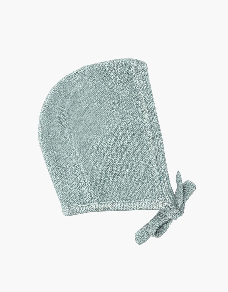 A Minikane Doll Clothing | Élie Blue Knit Bonnet with a light gray textured fabric, a rounded top, and a curved bottom edge featuring a fabric tie at the end, perfect for Minikane Babies. The bonnet appears to be made of soft, woven material. The background is plain white.