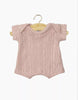 The Minikane 11" Doll Clothing Shorty Bodysuit in Dotted Knit - Petal is a light pink, short-sleeved cotton romper with a subtle dotted texture, shown on a wooden hanger against a plain white background.