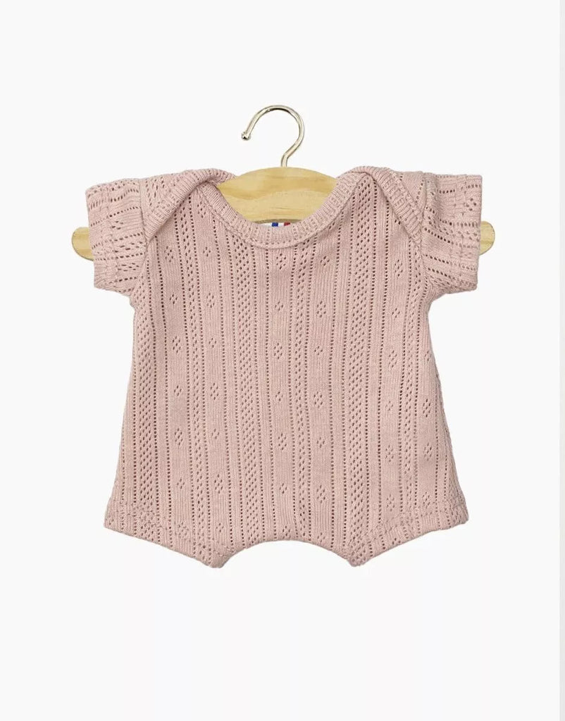 The Minikane 11" Doll Clothing Shorty Bodysuit in Dotted Knit - Petal is a light pink, short-sleeved cotton romper with a subtle dotted texture, shown on a wooden hanger against a plain white background.