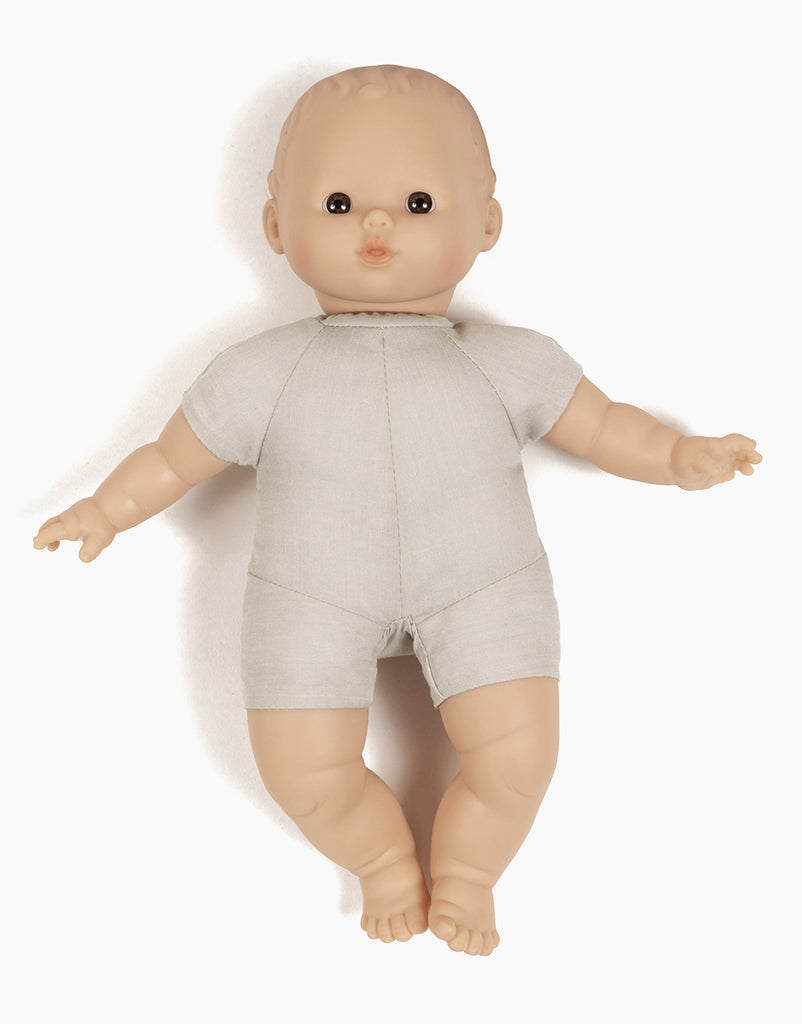 The Minikane Soft Body Doll (11") - Lucien features a light-skinned doll with short, light hair, dressed in a simple, light gray one-piece outfit. Crafted from phthalate-free vinyl, Lucien has a neutral facial expression and is shown lying down with arms slightly outstretched and legs relaxed—making it an ideal bedtime companion.