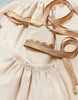 Close-up of a soft pink fabric with a gathered seam. Draped on the fabric are two decorative rose gold ribbons, one with a lace edge and the other plain. The materials suggest they could be for a whimsical children's costume or Minikane | Little Fairy Costume In Linen Ecru For Child and Doll accessories.