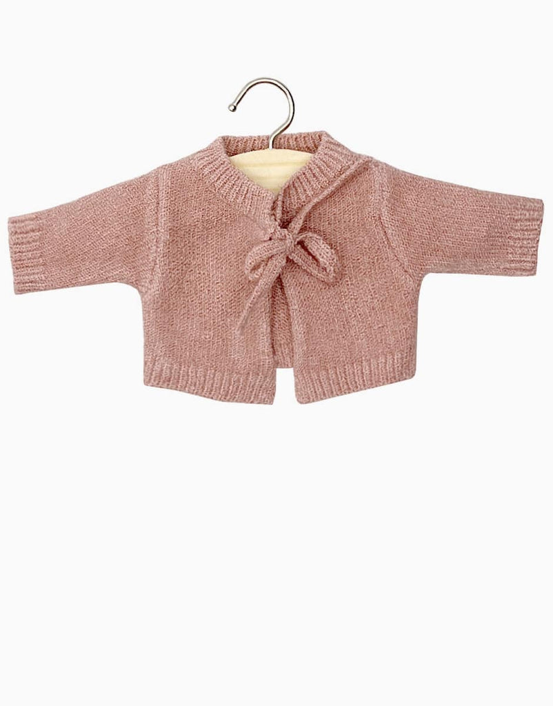 A small pink Minikane Doll Clothing | Tea Pink Knit Alix Cardigan displayed on a wooden hanger. The cardigan, perfect for Minikane Babies, features long sleeves, a V-neck, and a bow tie front closure. Hand washable and set against a plain white background.