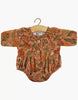 The Minikane Doll Clothing Leonore Ruffled Romper in Viscose - Birds of the Islands features long sleeves, a ruffled collar, wooden buttons, and a vibrant floral pattern, designed to fit Minikane Gordis dolls and displayed on a wooden hanger.