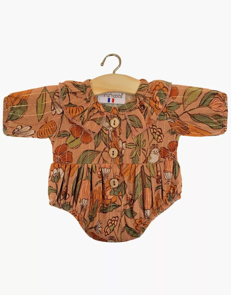 The Minikane Doll Clothing Leonore Ruffled Romper in Viscose - Birds of the Islands features long sleeves, a ruffled collar, wooden buttons, and a vibrant floral pattern, designed to fit Minikane Gordis dolls and displayed on a wooden hanger.