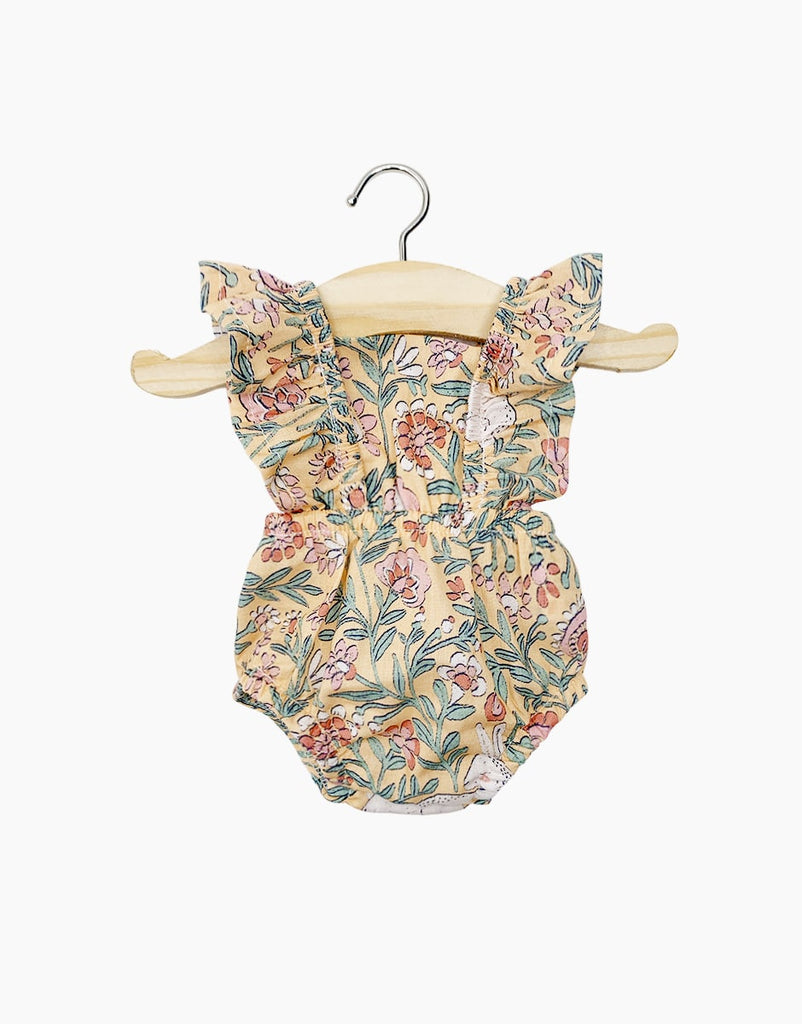 A Minikane | Lou Romper in Bohemian Bunny Doll Clothing with a floral pattern in various colors hangs on a wooden hanger with a metallic hook. Made from printed cotton, the romper features ruffled armholes and an elastic waistband. The background is plain white, reminiscent of retro romper styles perfect for Minikane Gordis dolls.