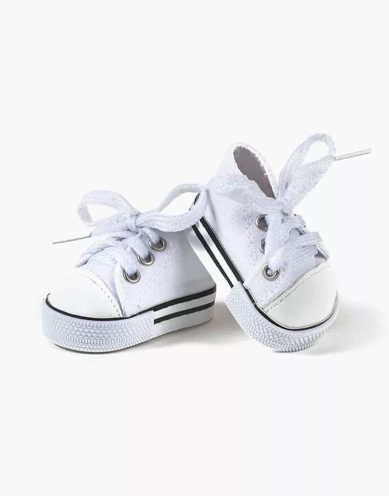 The Minikane Doll Shoes, Converse Style White Sneakers are a pair of small white baby sneakers featuring laces tied in bows. Designed in a classic Converse style, the shoes sport a black stripe around the rubber sole and metal eyelets for the laces. Perfectly scaled for Minikane Gordis dolls, they are positioned against a plain white background.