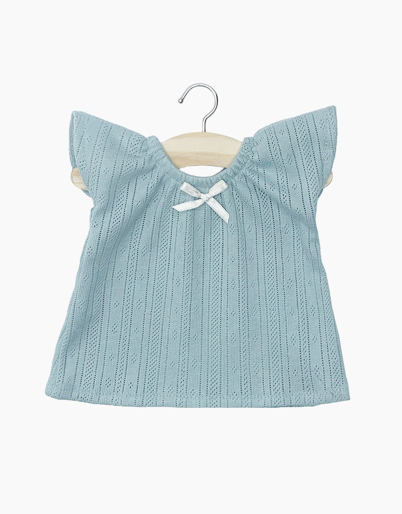 A Minikane Clothing| Nightgown in Peacock Blue adorned with small, vertical eyelet designs. Perfectly sized for 34 & 37cm dolls, this adorable piece is displayed on a wooden hanger and features a white bow at the neckline. The background is white.