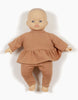 A baby doll from the Minikane Babies dolls collection, with light skin and blue eyes, is dressed in the Minikane Clothing | Ophélia Set in Brown Sugar—a brown outfit consisting of a long-sleeve top and matching pants. The cotton hand-washable doll has no hair and is posed with its arms slightly out to the sides against a plain white background.