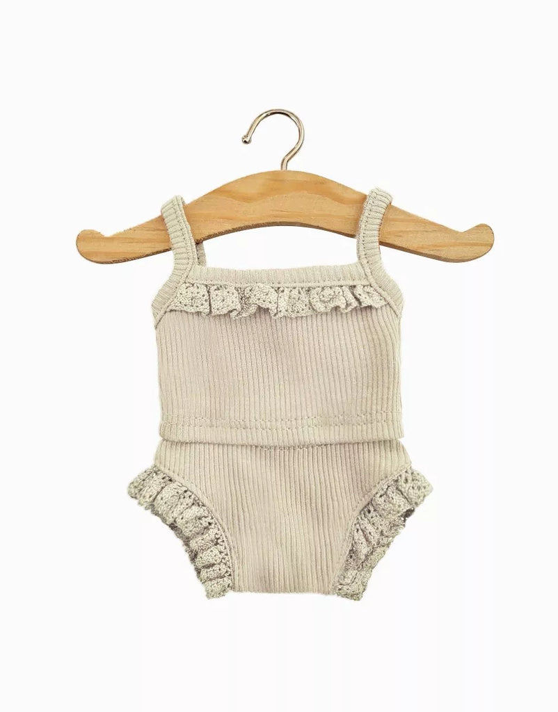 A Minikane Doll Clothing | Les P'tits Basique Girls' Underwear in ribbed linen knit and lace featuring a beige baby romper with spaghetti straps and ruffled trim on the chest and leg openings, hanging on a wooden hanger against a white background. The ribbed fabric adds texture and style reminiscent of popular Minikane Gordis dolls.