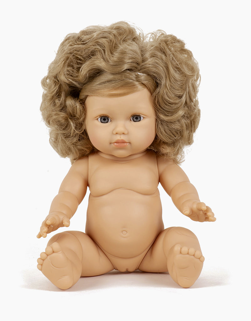 A Minikane Baby Doll (13") - Lola with curly blond hair is seated against a plain white background. The anatomically correct doll has blue eyes, a slightly open mouth, and chubby limbs with visible toes and fingers, emanating a natural vanilla scent.